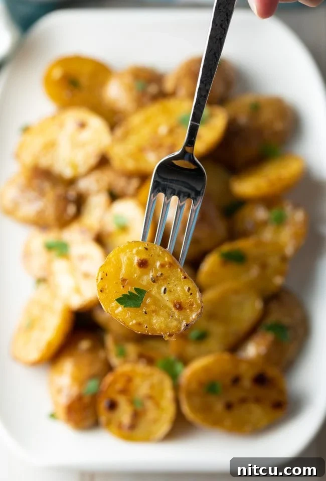 Close up of a fork holding up a garlic potato with parsley sprinkled on it.