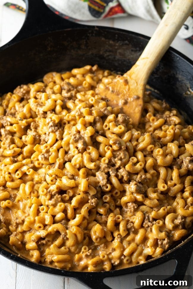 A wooden spatula stirring homemade cheeseburger macaroni in a single pot, showcasing the ease of this one-pot meal.