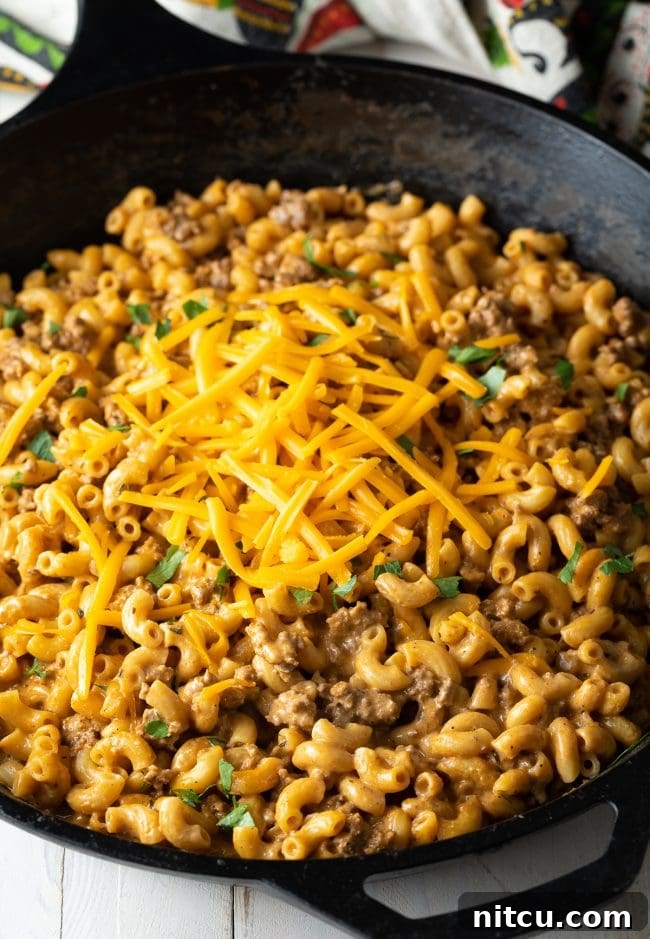 A large skillet of homemade cheeseburger mac and cheese, generously garnished with fresh chopped parsley and a sprinkle of shredded cheddar.