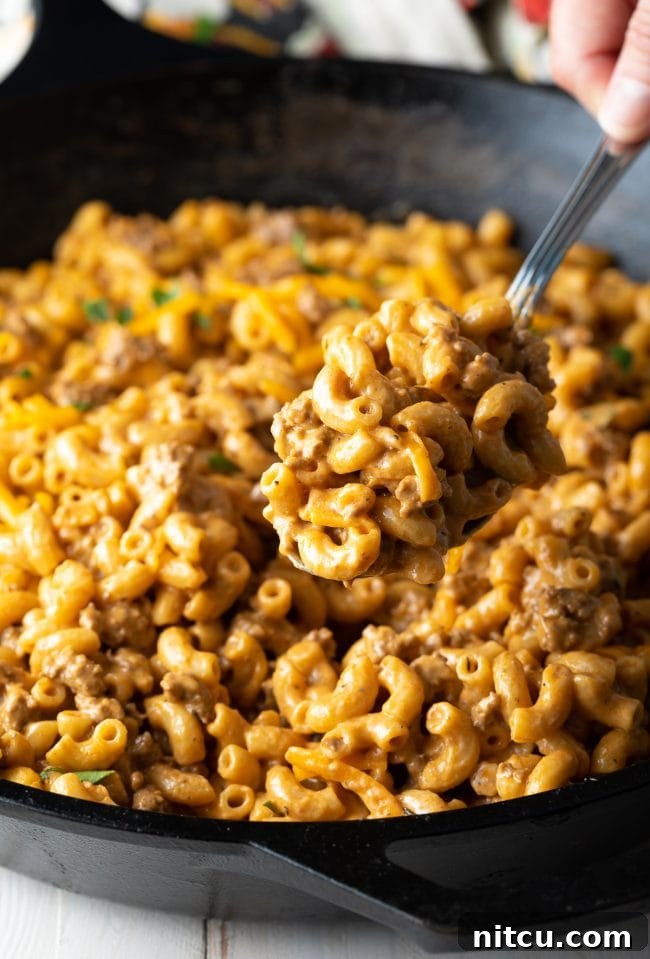 A serving spoon lifting a portion of cheesy homemade hamburger helper from the skillet, ready to plate.