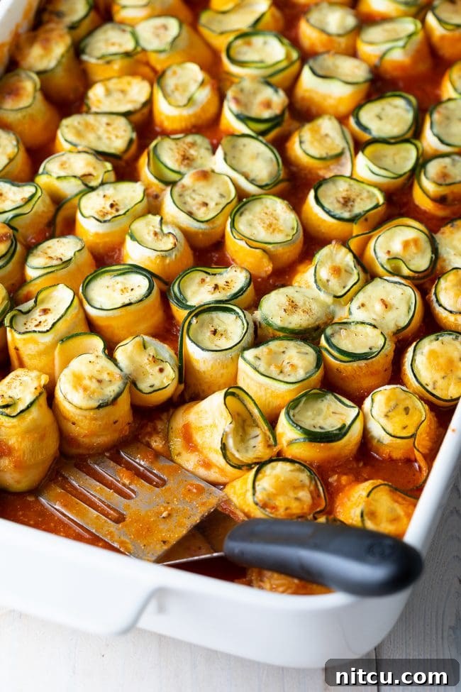 Keto zucchini lasagna roll ups in a baking dish with a spatula ready to serve. 