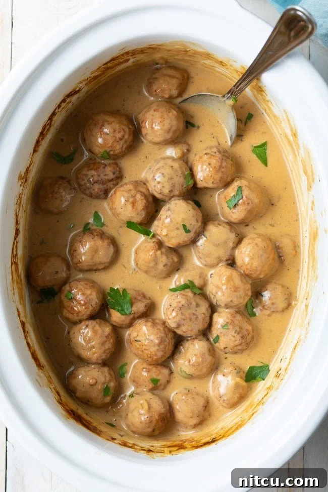 Overhead shot of perfectly cooked Swedish Meatballs simmering in their creamy, rich sauce within a slow cooker.