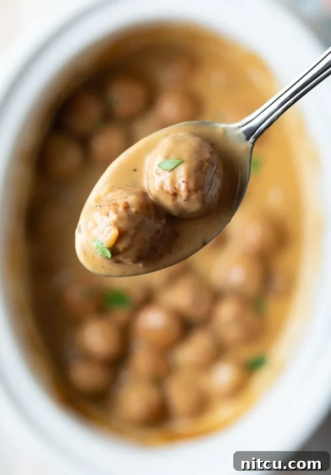 Instant Pot Swedish Meatballs being lifted out of the pot with a serving spoon, showcasing the rich, creamy sauce clinging to each meatball.