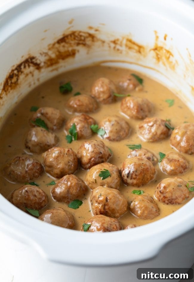 Close-up of Crockpot Swedish Meatballs garnished with vibrant fresh chopped parsley, ready to be enjoyed.