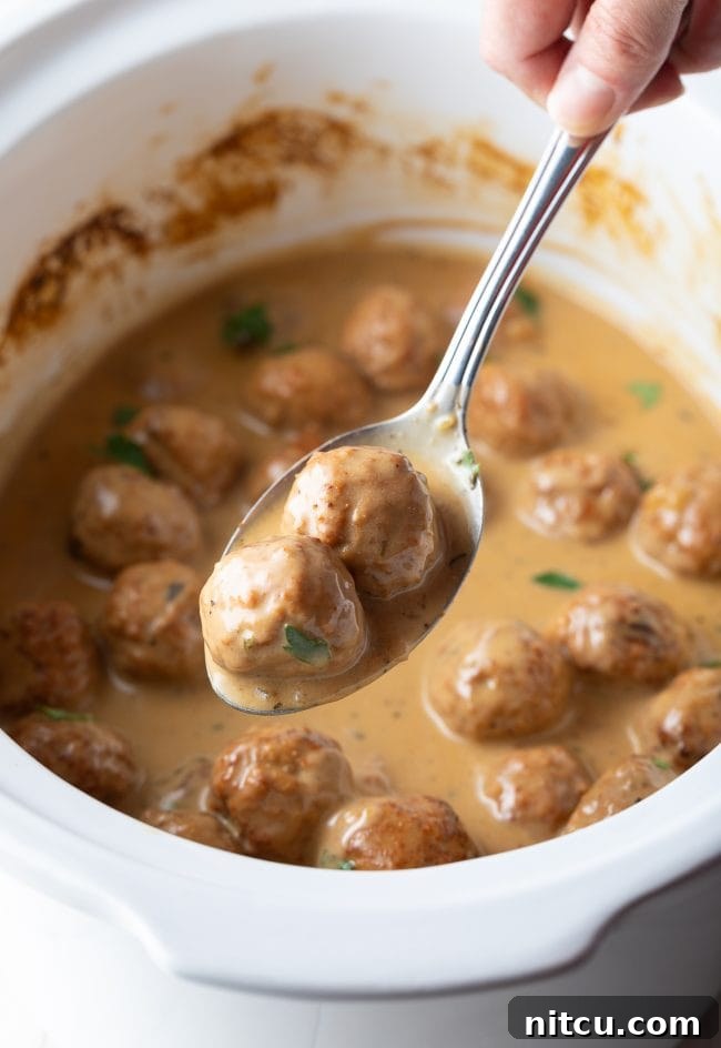 A serving spoon lifting a creamy Swedish meatball from the slow cooker, ready to be plated for a delicious meal.