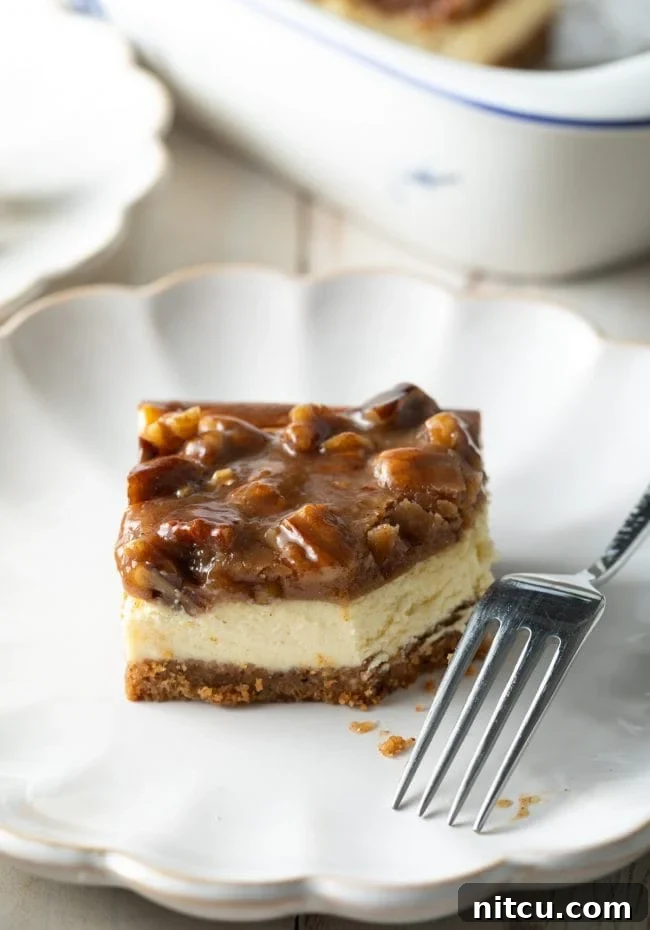 A beautifully presented slice of Pecan Pie Cheesecake with caramel pecan topping on a plate, with a fork beside it, indicating a bite has been taken.