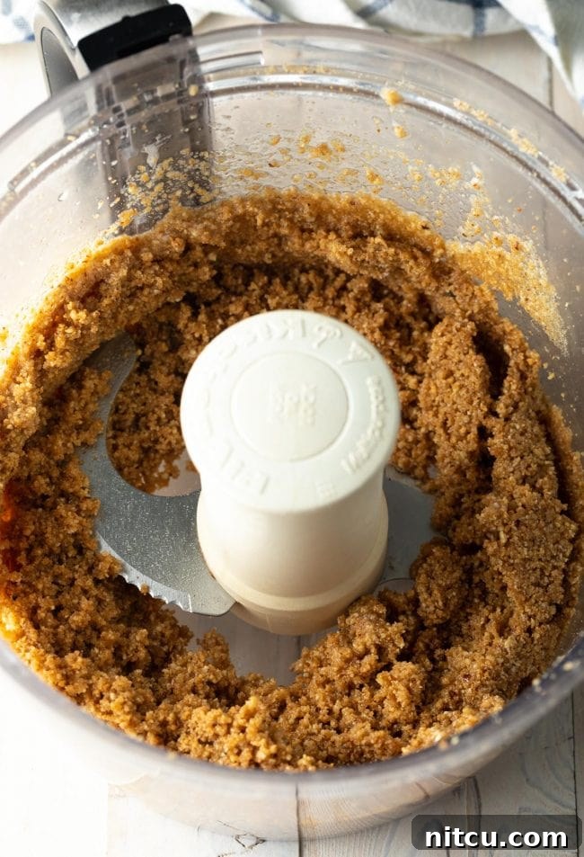 The graham cracker crust mixture being pulsed in a food processor, showing the crumbs being formed.