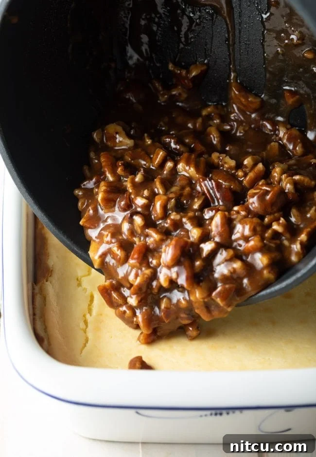 Gooey pecan caramel topping being carefully poured and spread over the baked cheesecake in a baking dish.