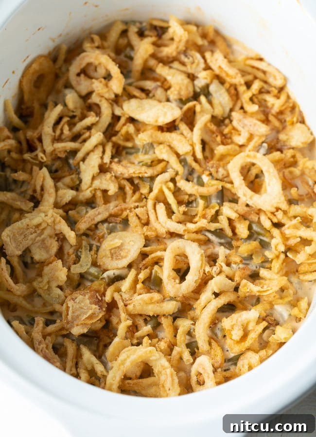 Hearty Green Bean Casserole simmering in a slow cooker, featuring a rich, creamy sauce and ready for its crispy onion topping.