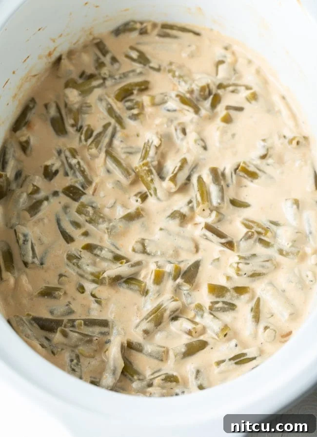 Crockpot Green Bean Casserole with cream cheese bubbling gently in the slow cooker, perfectly cooked and ready for its final topping.
