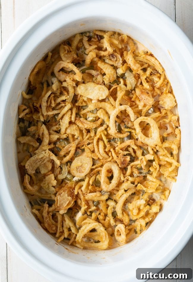 A large serving dish of the best Green Bean Casserole from scratch, freshly made and topped with an abundance of golden-brown crispy fried onions.