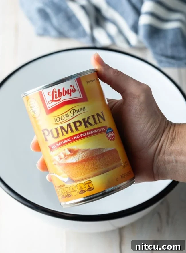 Hand holding a can of pumpkin over a mixing bowl. 