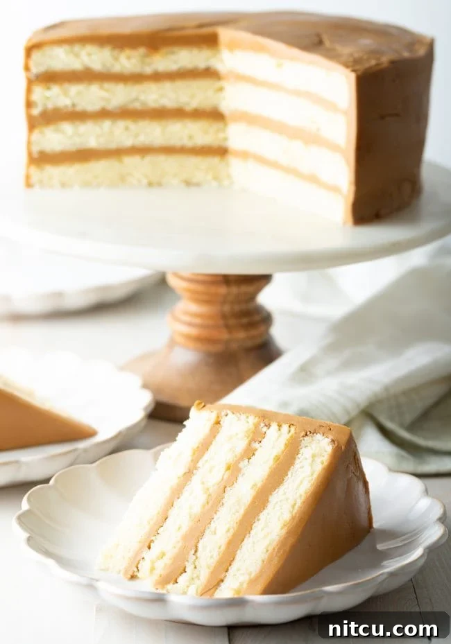 Southern caramel cake with salted caramel frosting on a cake stand with a piece of cake on a plate, ready to be enjoyed.