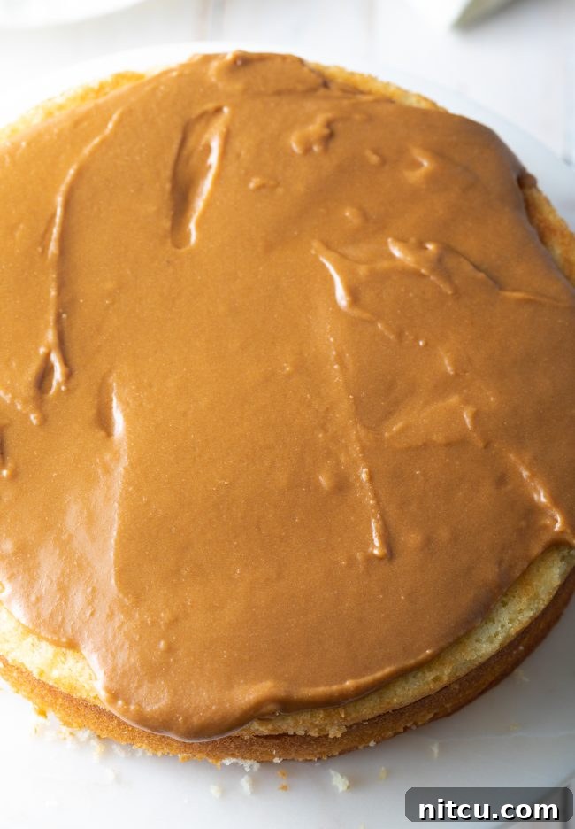 A layer of thick, spreadable caramel frosting being applied evenly to a cake layer, highlighting its rich consistency.