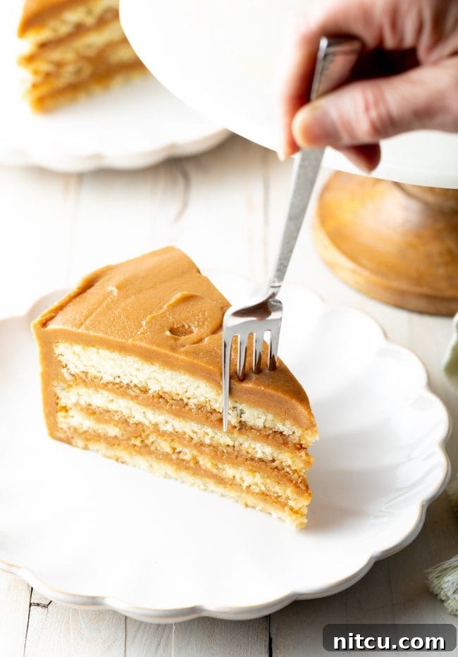 A close-up of a slice of Southern caramel cake, showcasing four distinct layers of white cake generously frosted with thick salted caramel, with a fork poised for a bite.