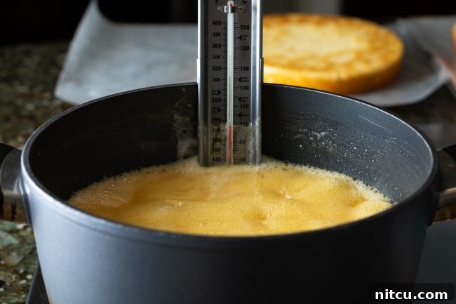 A large pot of caramel ingredients simmering on the stove with a candy thermometer clipped to the side, crucial for making perfect caramel frosting.