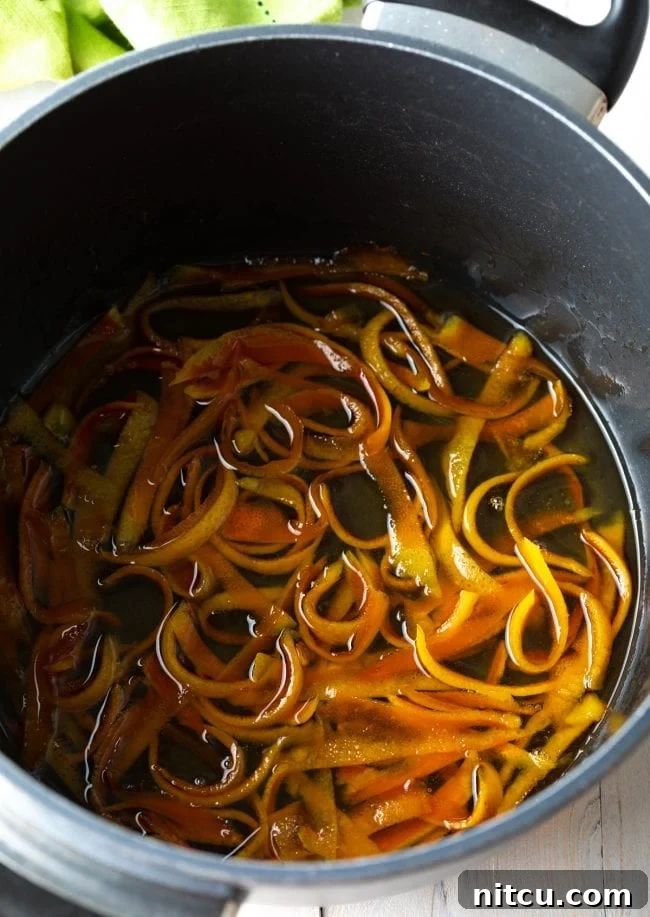 Orange peels gently simmering in a sweet syrup, illustrating the candying process.