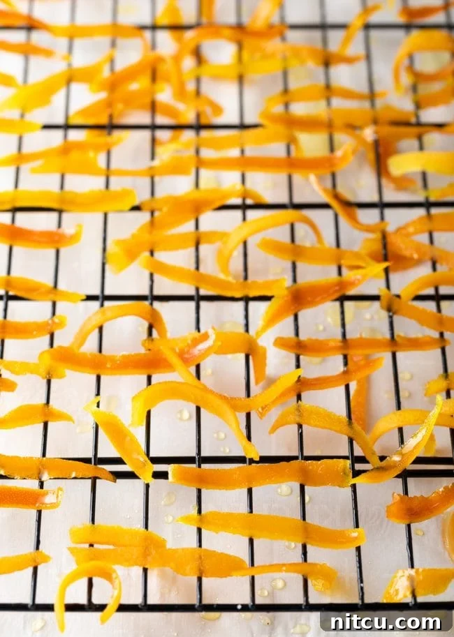 Freshly candied orange peels laid out on a drying rack, allowing excess syrup to drain and setting their sugary coating.