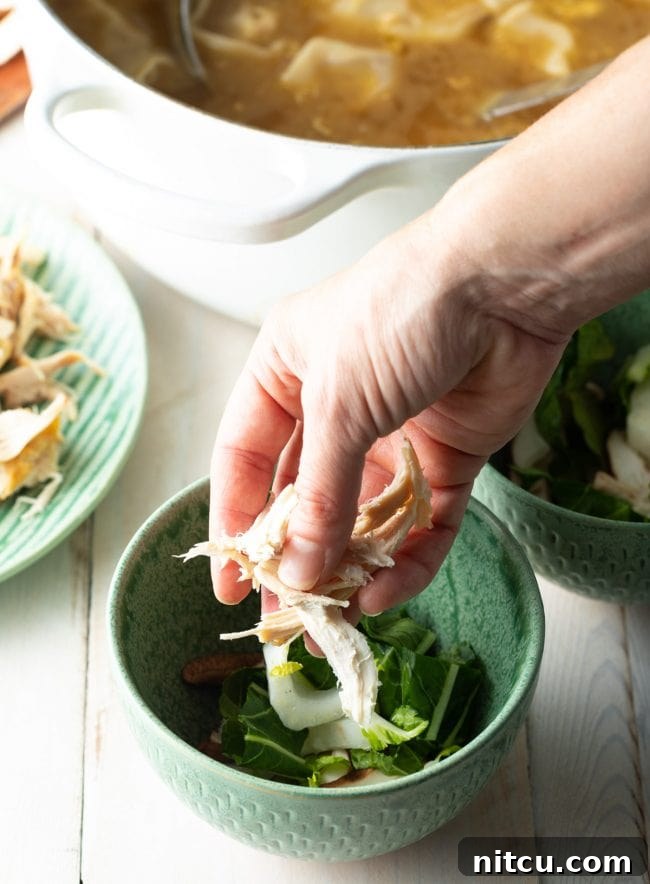 Shredded chicken and fresh vegetables being arranged in soup bowls, ready for the hot broth.