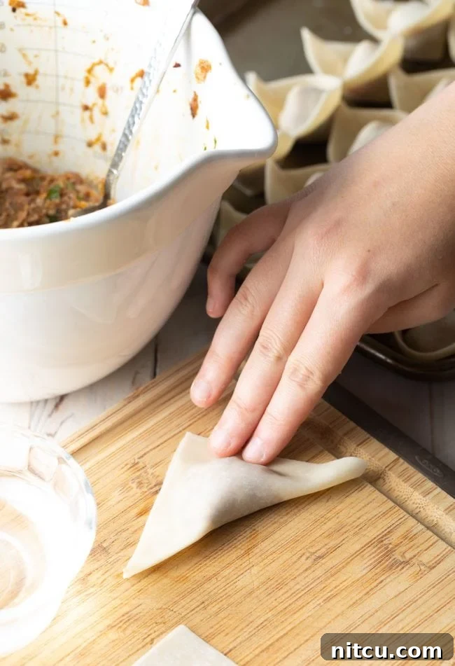 Demonstration of folding wontons, showing the process of bringing the two bottom corners together to seal.
