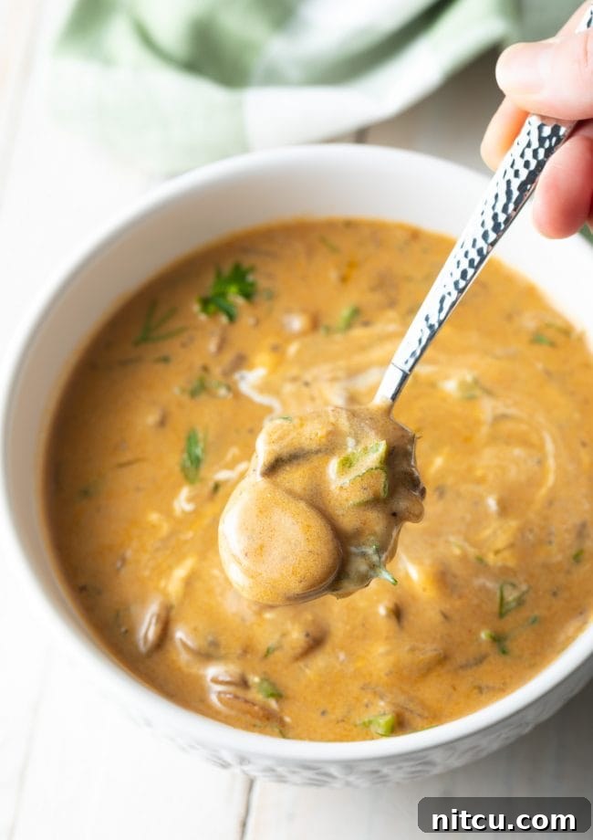 A spoon scooping up a generous portion of gluten-free vegetarian mushroom soup, highlighting its creamy texture.