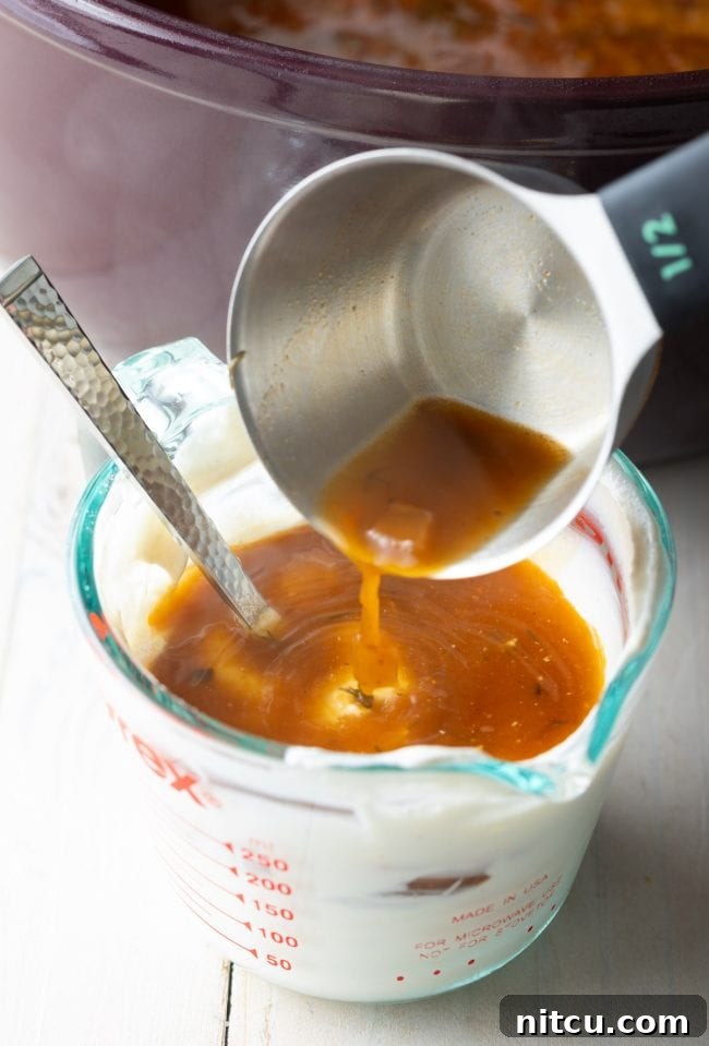 Mixing hot soup broth into a bowl of cashew cream to temper it for a vegan soup base.