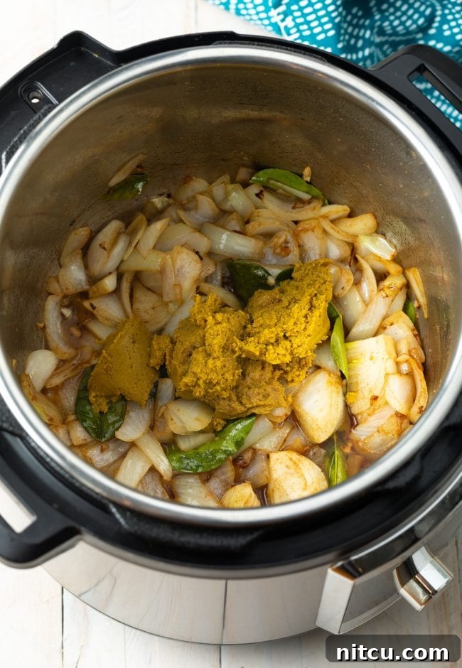 Overhead shot of onions, garlic, and kaffir lime leaves sautéing in the Instant Pot with green curry paste.