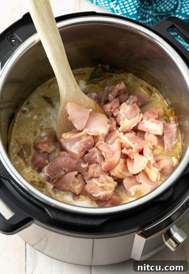 Diced chicken pieces being added to the Instant Pot, ready to be coated in the curry base.