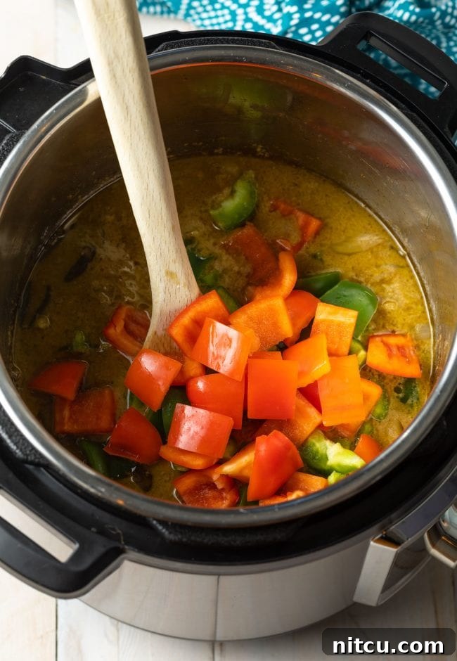 Red and green bell peppers being added to the simmering green curry in the Instant Pot.