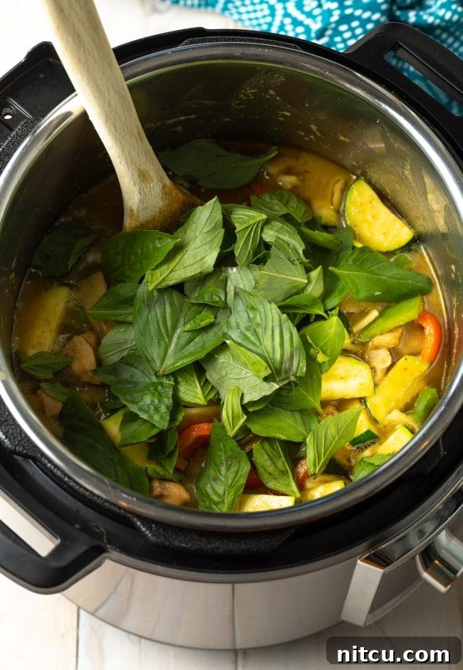 Fresh Thai basil leaves being stirred into the finished Instant Pot Green Curry.