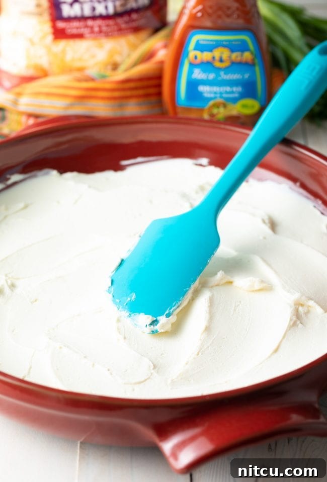 Using a blue spatula to spread cream cheese into a red pizza pan.