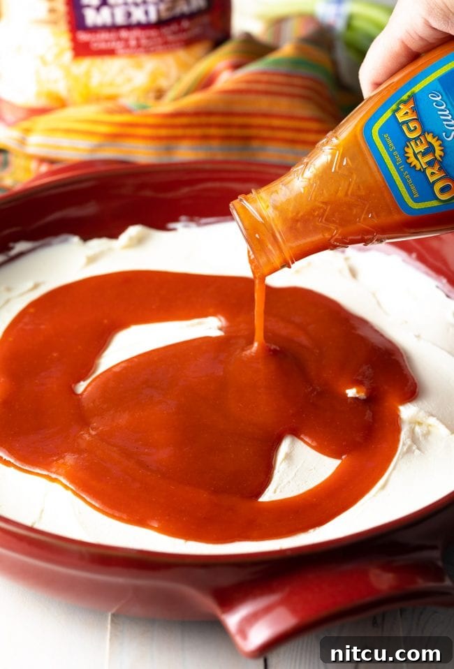 Pouring enchilada salsa over cream cheese spread into a red round baking dish.