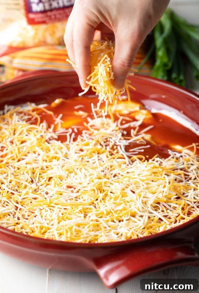 Hand sprinkling shredded cheese onto the enchilada sauce.