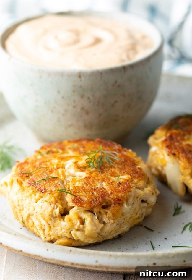 Crab cakes on a plate with a sprinkle of dill on top. 