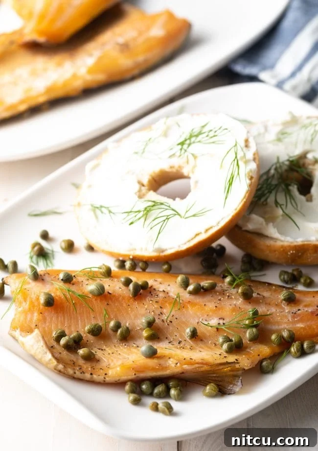 A beautifully arranged platter with smoked trout covered in dill and capers, surrounded by bagels topped with cream cheese and other garnishes.