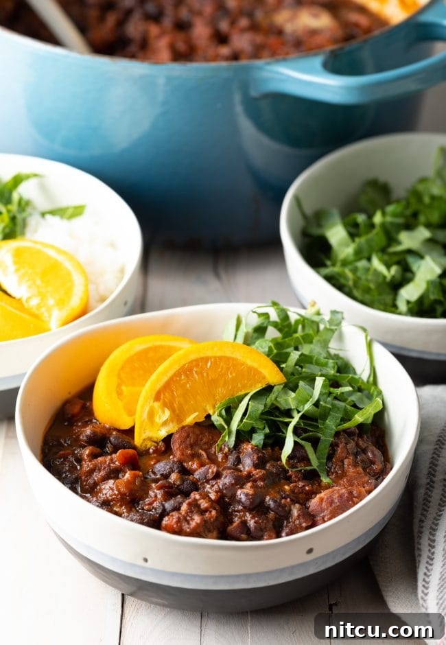 A bowl of pork and black bean stew topped with orange slices and shredded greens. Bowls of extra garnishes and the soup pot are in the background.
