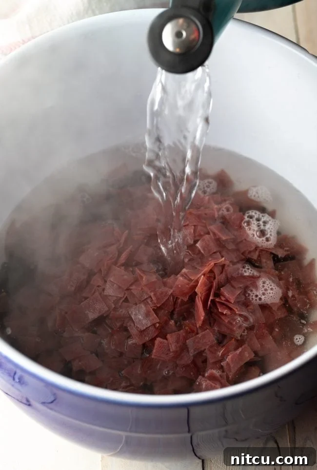 Shredded beef and black beans in a stew pot with boiling water pouring on top.