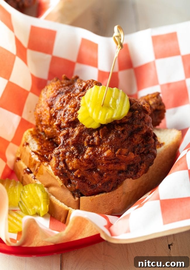 A basket of Nashville hot chicken, perfectly spiced and golden, served on white bread with dill pickles on top.