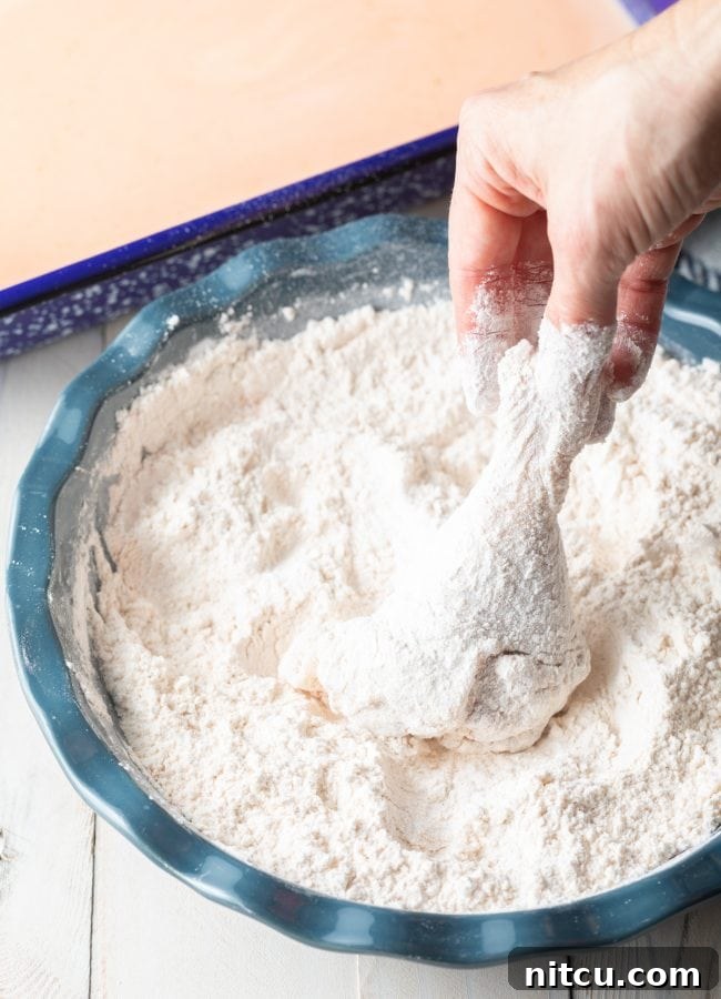 Raw chicken pieces being thoroughly coated in a dry flour mixture, ensuring a perfect crispy crust.