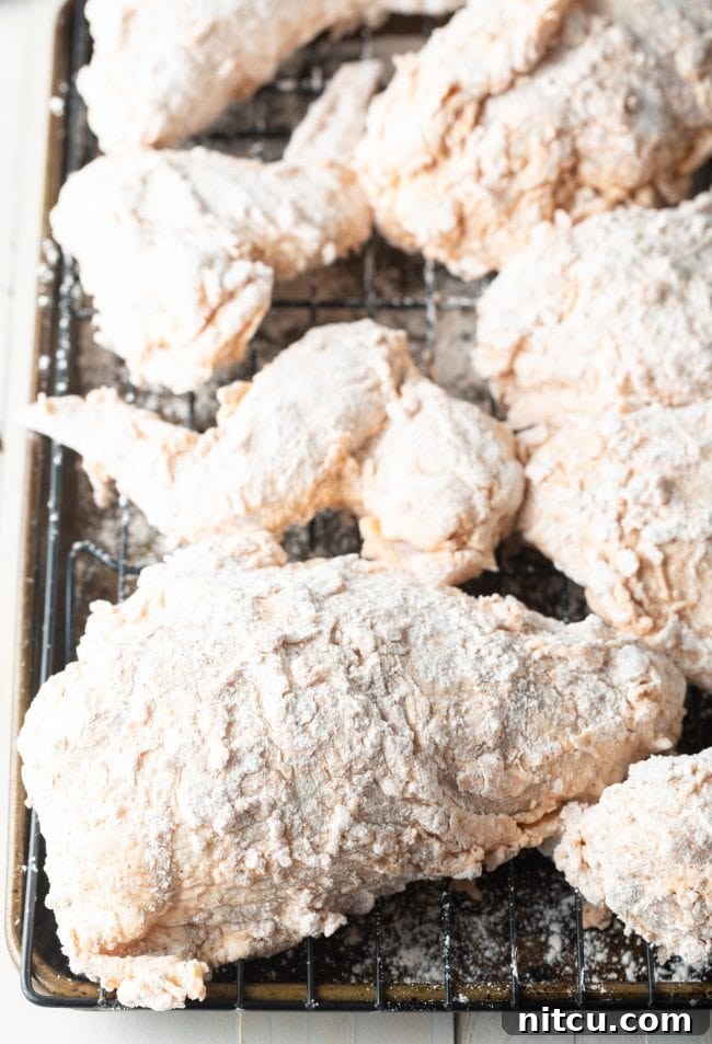 Breaded chicken pieces resting on a wire rack, allowing the coating to adhere properly before frying.