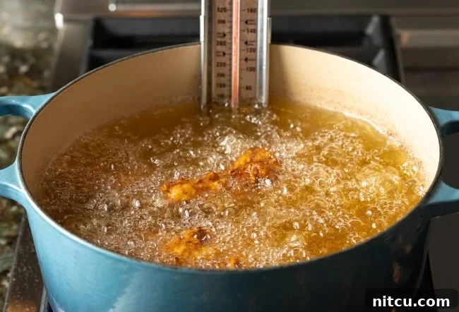 Several pieces of chicken sizzling and frying in a pot of hot oil, turning golden brown.