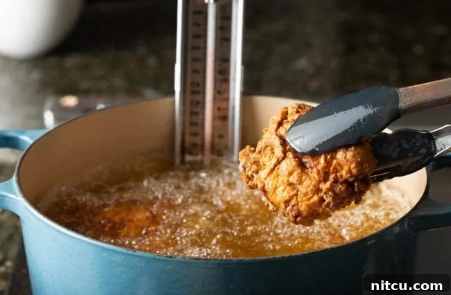 Golden-brown fried chicken being carefully lifted out of hot oil with tongs, showcasing its crispy texture.