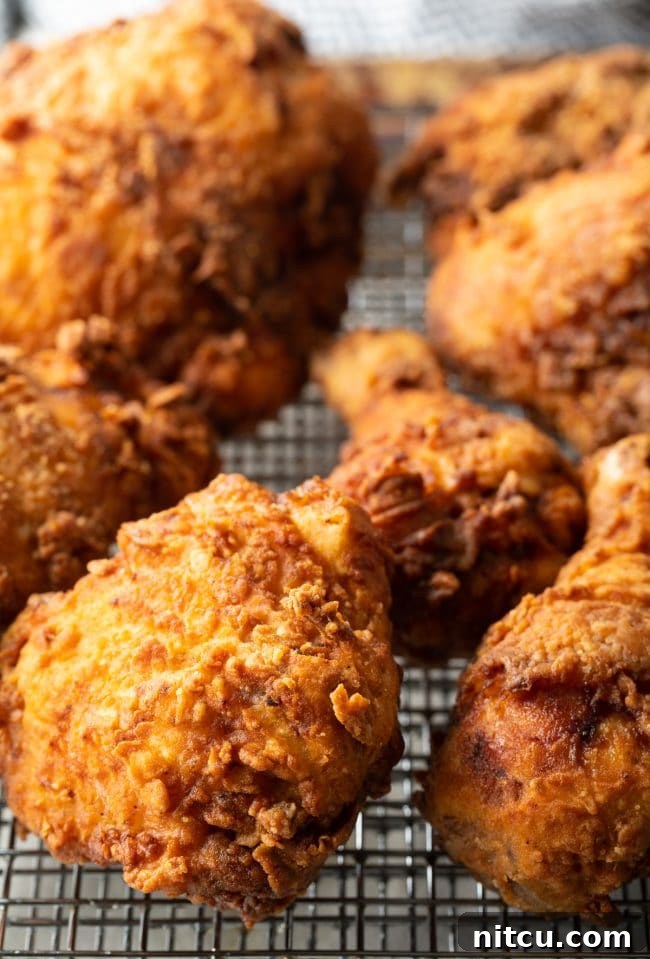 Freshly fried chicken pieces resting on a wire rack, allowing excess oil to drain and maintain crispness.