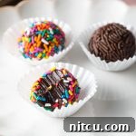 A close-up image of two brigadeiros, one covered in chocolate sprinkles and the other in colorful rainbow sprinkles, showcasing their appealing texture and vibrant decoration.