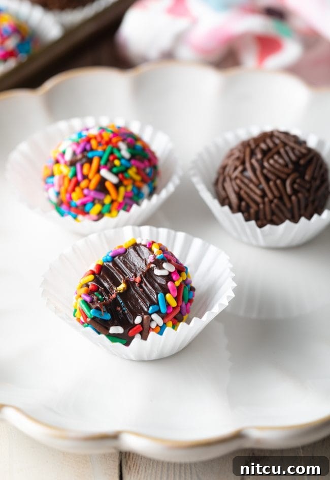 Close up shot of three perfectly round Brazilian truffles plated with one half eaten, revealing its soft, fudgy interior, on a white plate.