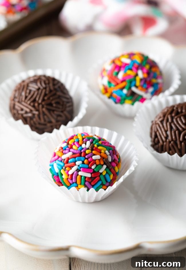 Closeup of 4 brigadeiros on a serving plate, each perfectly round and covered in colorful sprinkles, ready to be enjoyed.