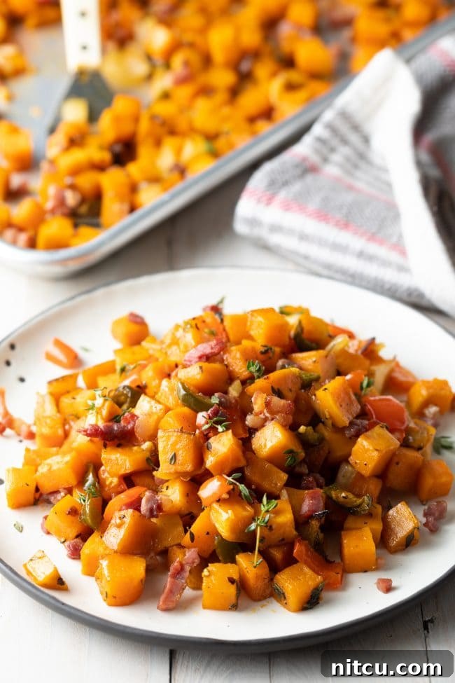 Sweet potato hash browns served on a white plate, with a baking sheet filled with more hash browns visible in the background, showcasing their golden-brown texture.