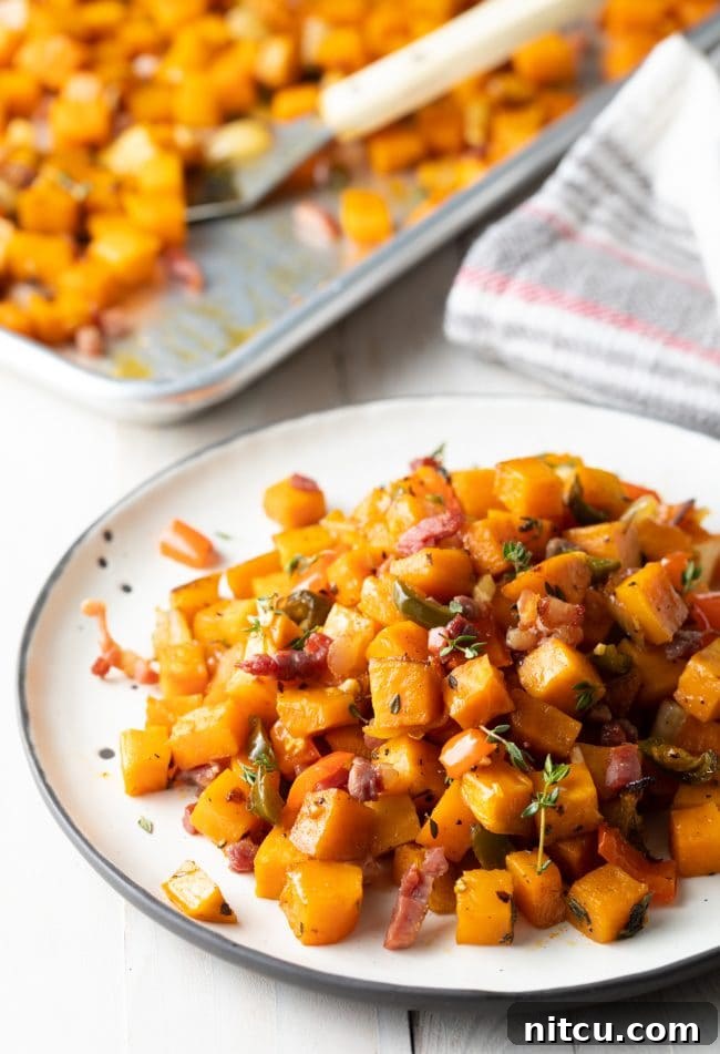 A white plate holding a generous serving of sweet potato hash browns, with a blurred background showing a baking sheet full of the same delicious dish.