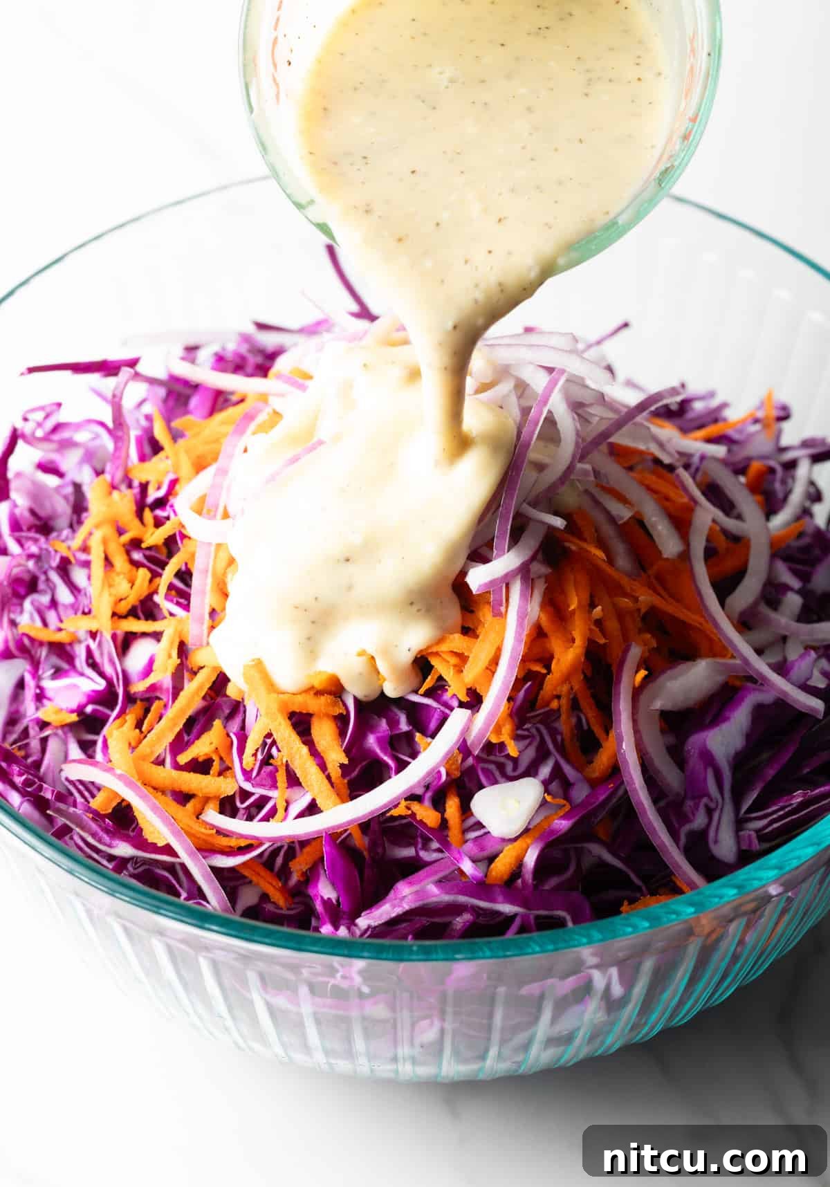 A mayonnaise mixture is being poured over a red cabbage slaw recipe.