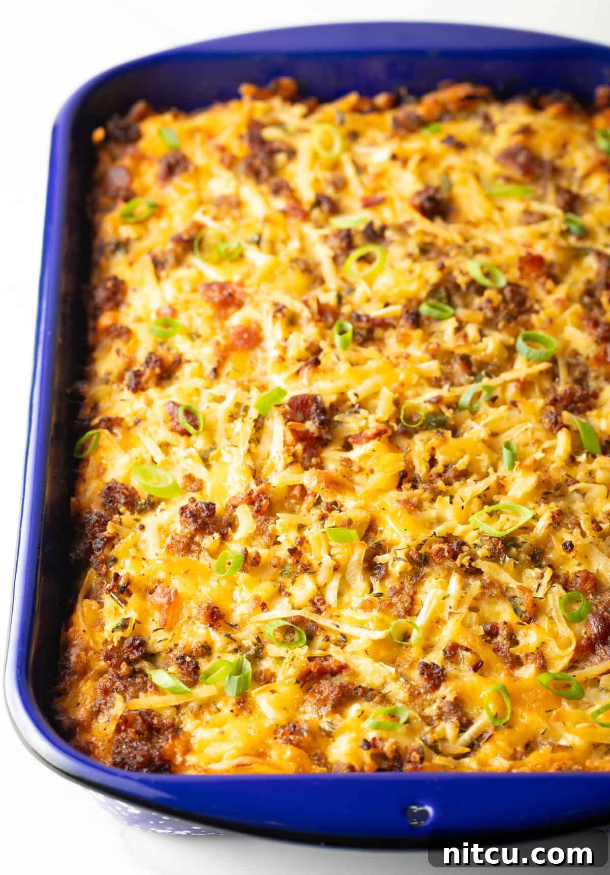 A freshly baked breakfast casserole with hash browns, boasting a golden-brown and bubbly top, rests invitingly in a blue baking dish.